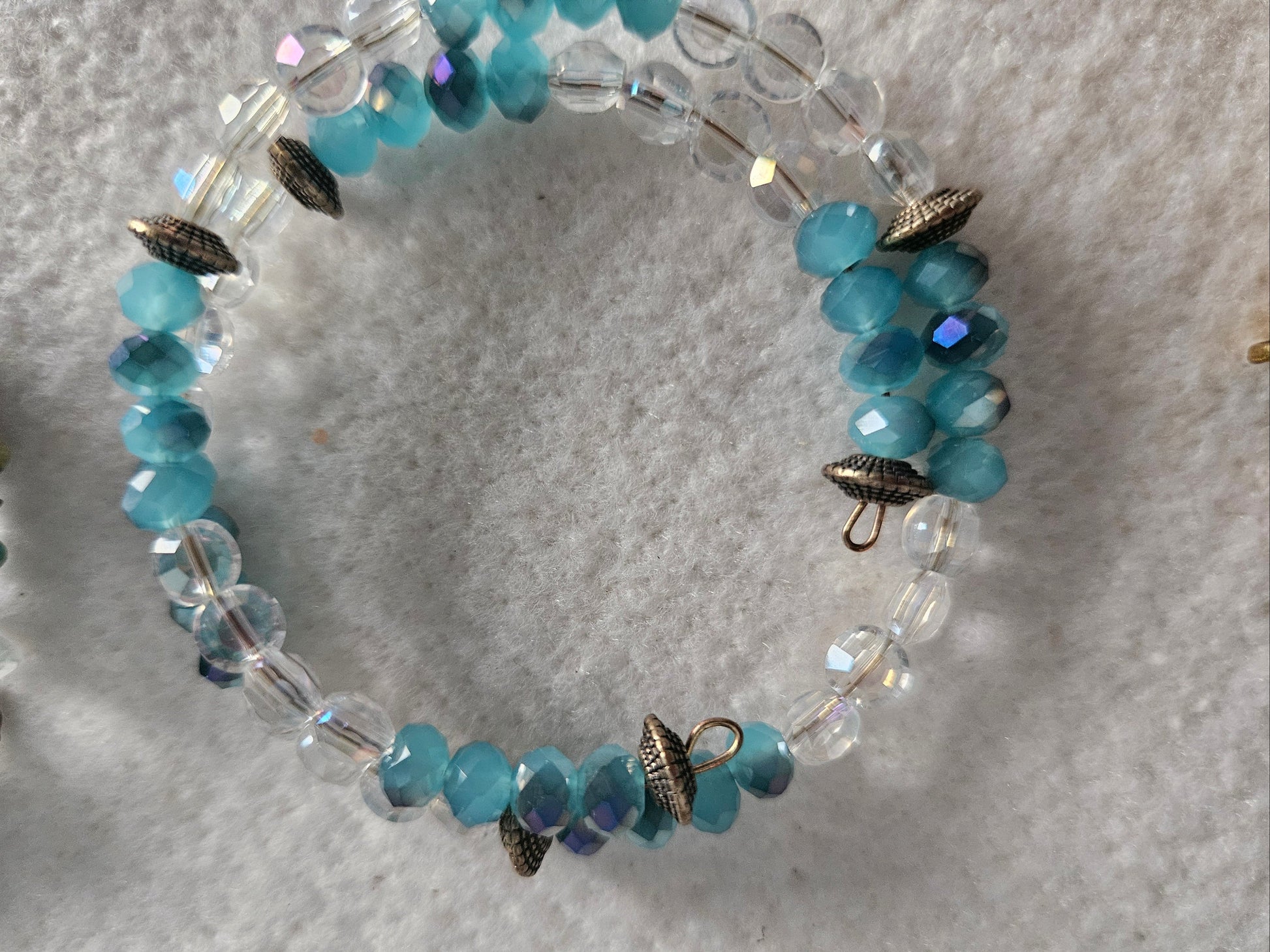 A beaded stretch bracelet featuring faceted light blue beads, clear faceted beads, and small metallic bronze arrowhead charms, displayed on a textured white fabric background.